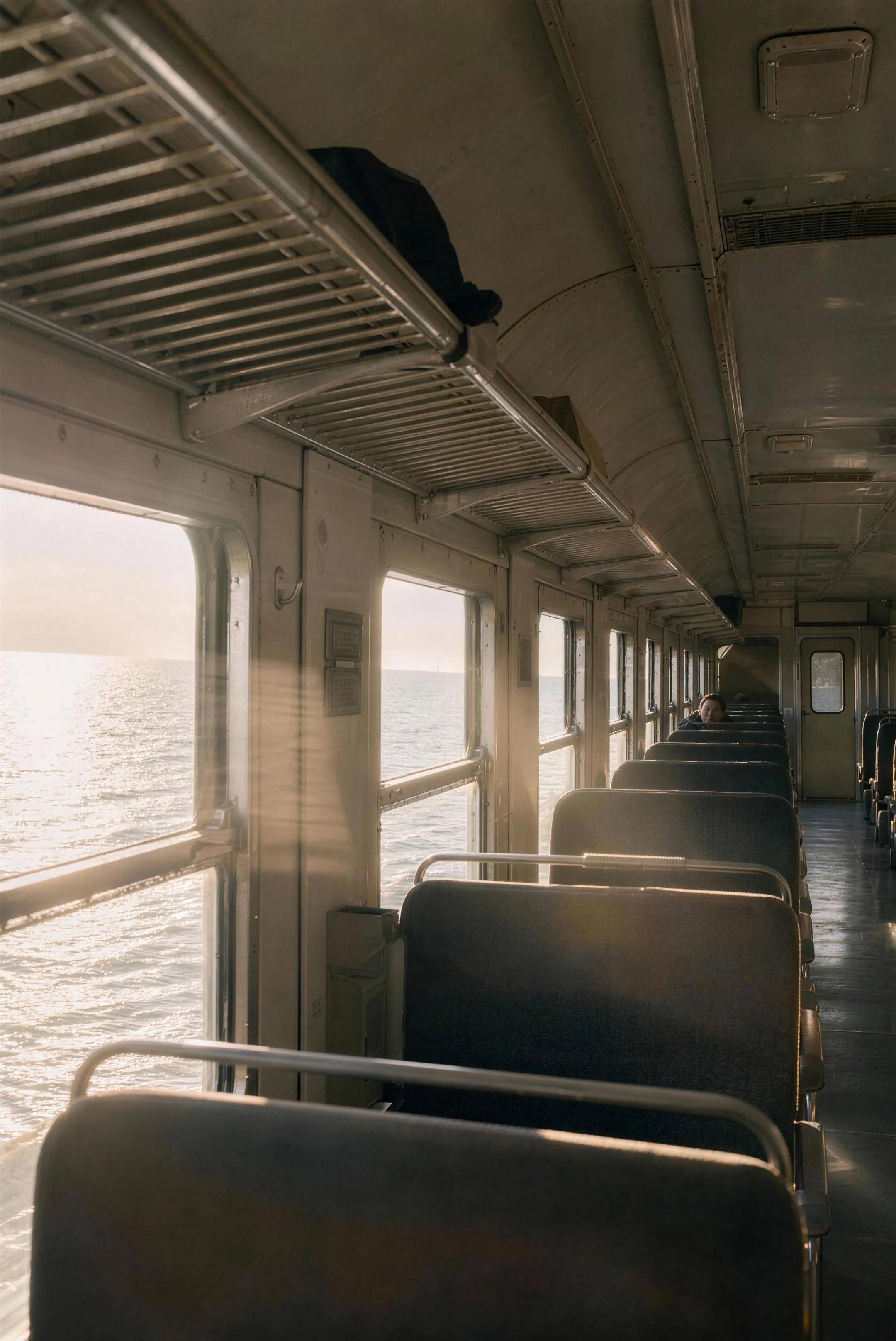 A shaft of low winter sun cutting across the worn seats of an old commuter train, dust in the light, the flat sea sliding past the windows